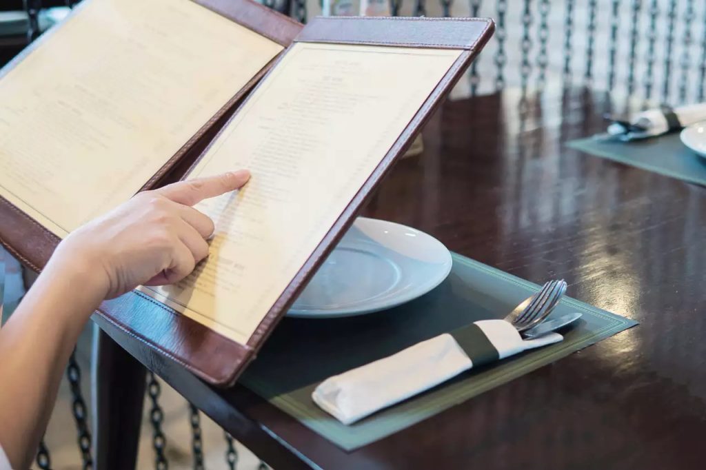 Cliente analisando cardápio físico em restaurante, destacando a importância do posicionamento estratégico dos itens em um cardápio para bares
