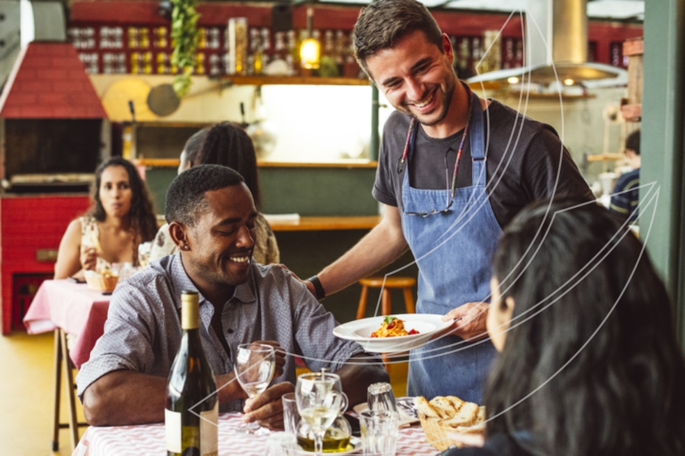 Garçom sorridente servindo um prato de comida a clientes em restaurante aconchegante, ilustrando atendimento de qualidade e experiência positiva.”